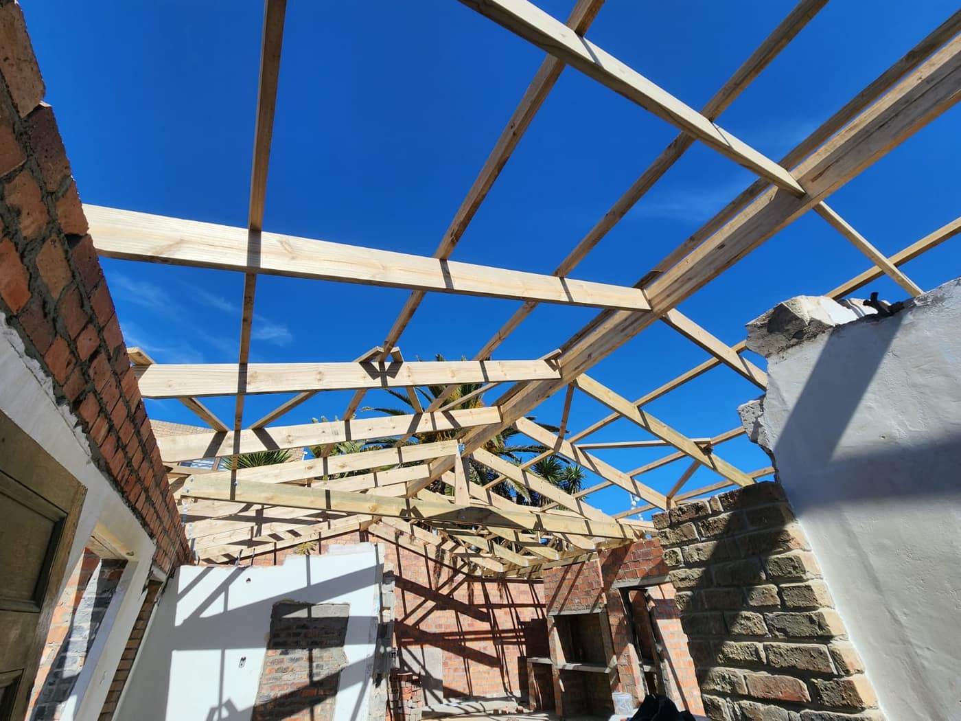 Looking up at the braced timber roof structure against a blue sky