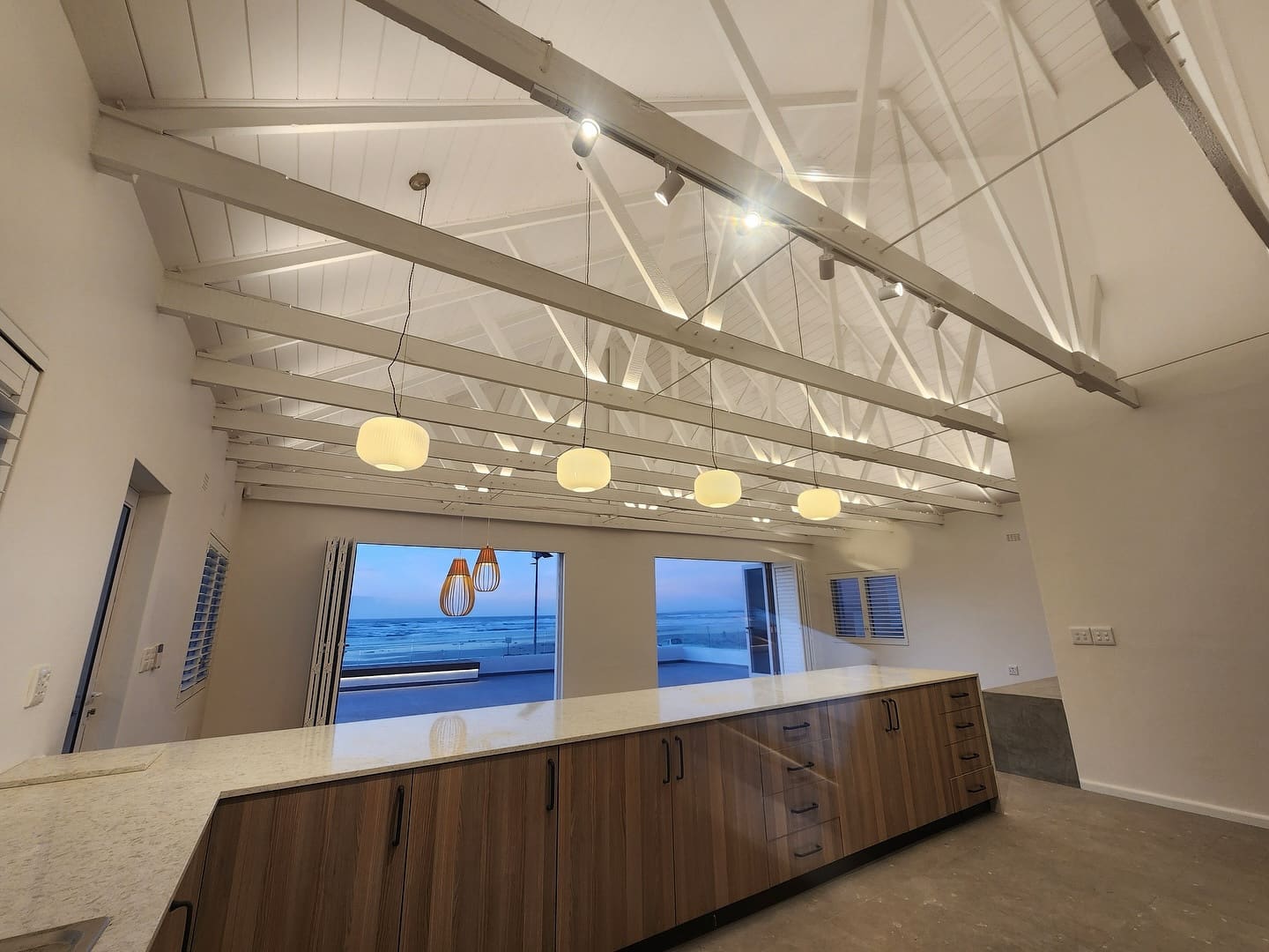 Renovated coastal kitchen with a stone-topped island, timber cabinetry and folding doors onto the sea